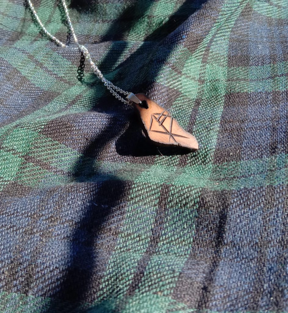 Driftwood pendant with the symbol for the wolf on it.